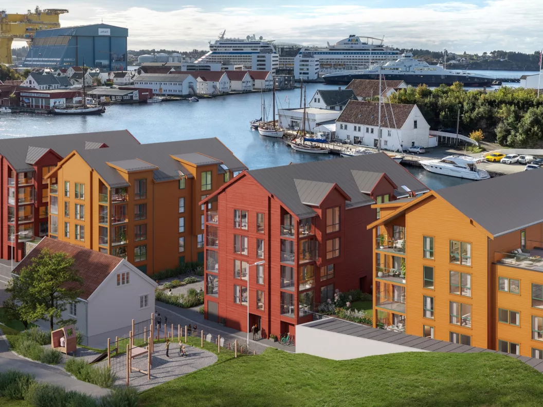 Fargerike bygårder nær en vannkant med skip og et verft i bakgrunnen under en delvis overskyet himmel.