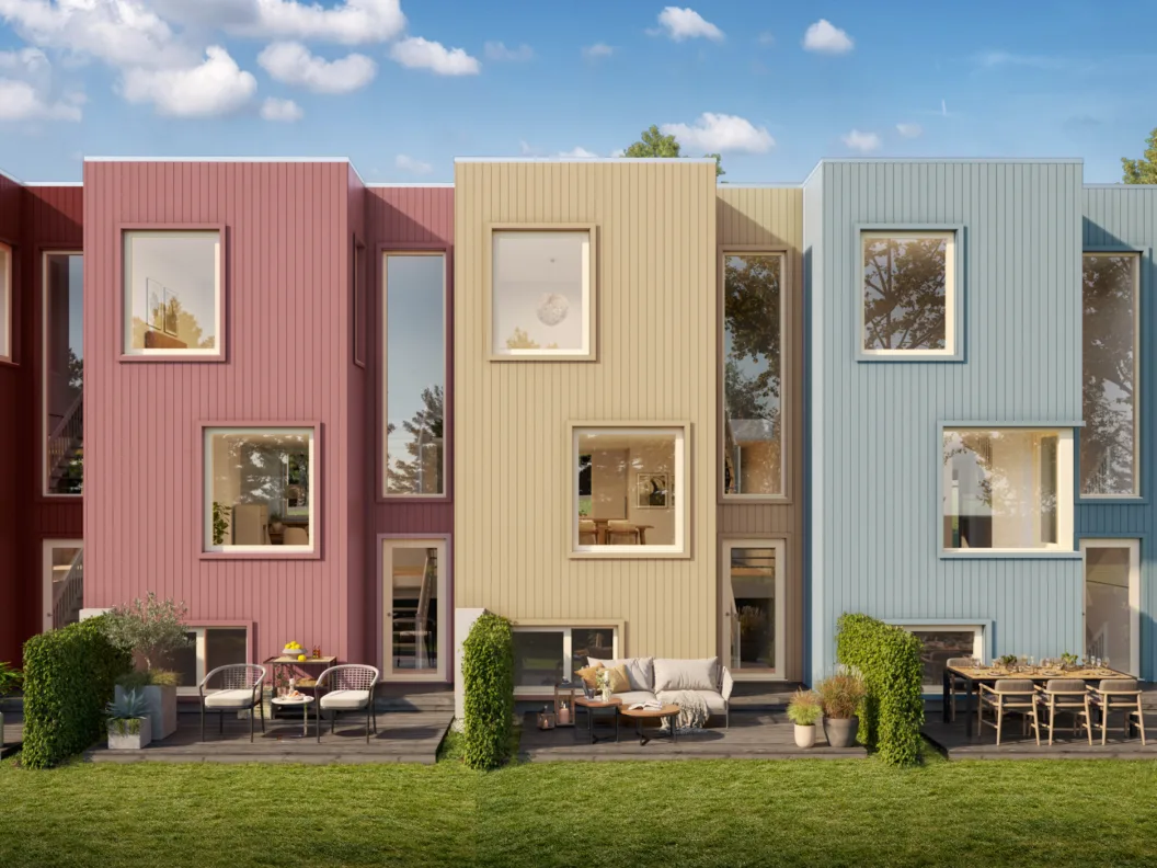 En rekke moderne, fargerike rekkehus med store vinduer, uteservering og grønne plener under en blå himmel.