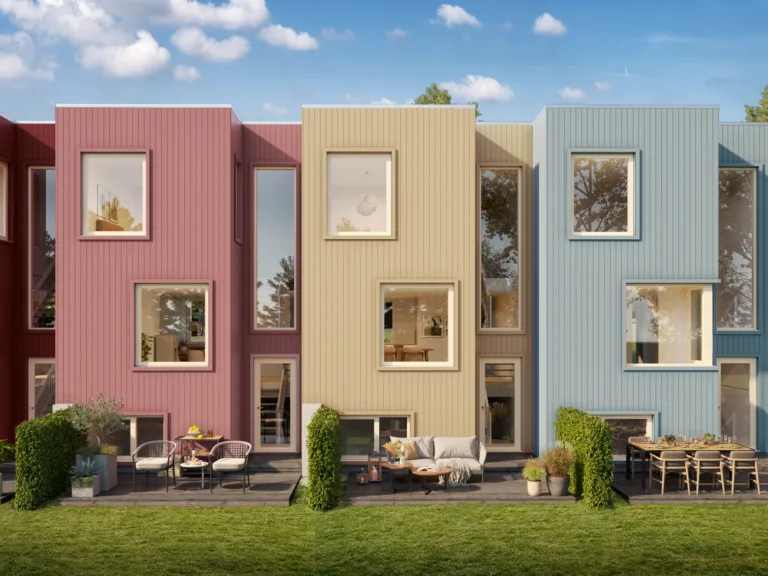 En rekke moderne, fargerike rekkehus med store vinduer, uteservering og grønne plener under en blå himmel.