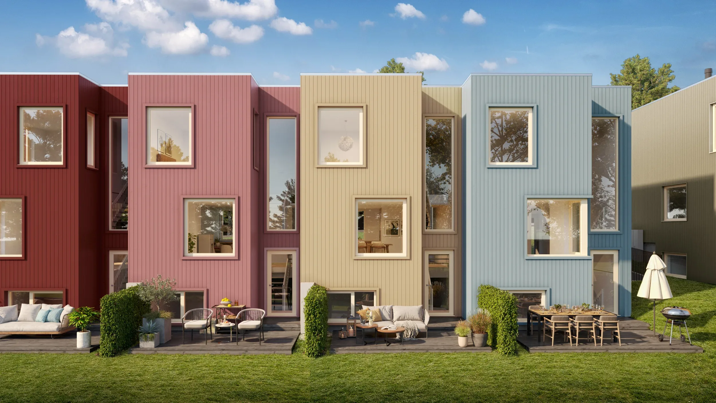 En rekke moderne, fargerike rekkehus med store vinduer, uteservering og grønne plener under en blå himmel.