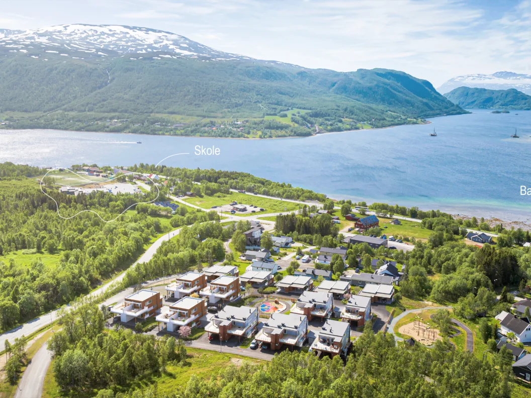 Flyfoto av en liten by nær en fjord med fjell i bakgrunnen; etiketter viser hvor en skole og en barnehage ligger.
