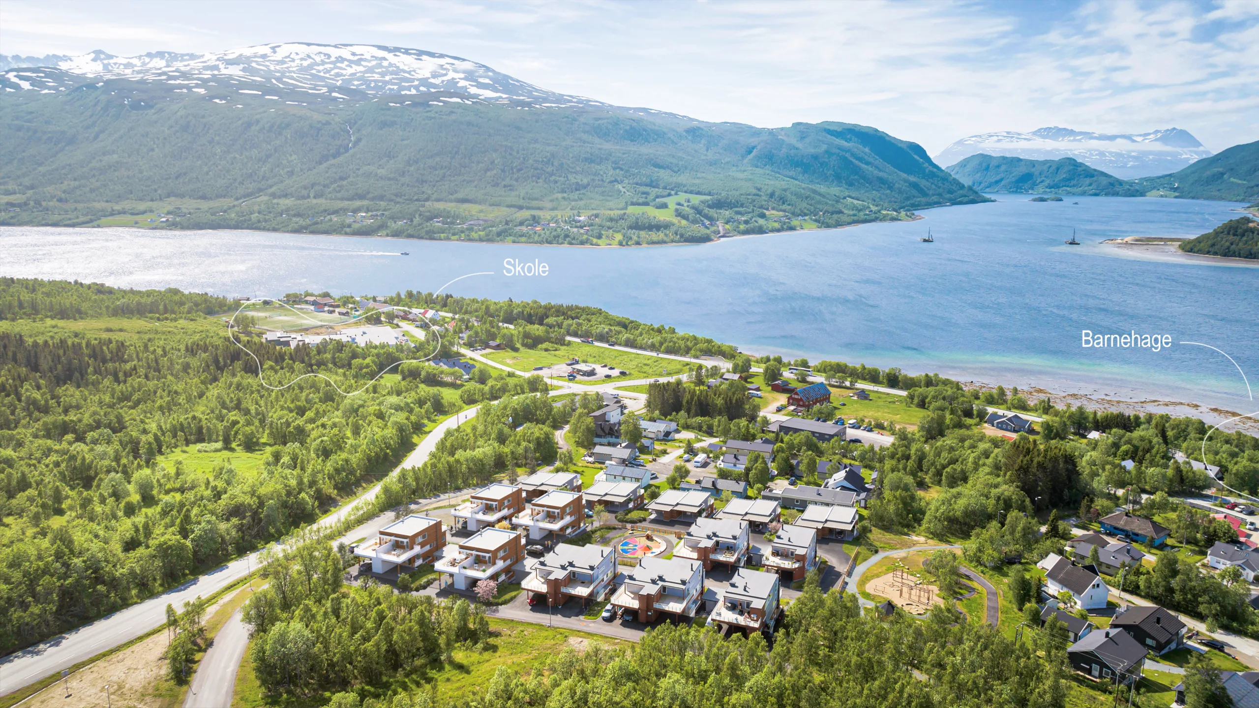 Flyfoto av en liten by nær en fjord med fjell i bakgrunnen; etiketter viser hvor en skole og en barnehage ligger.