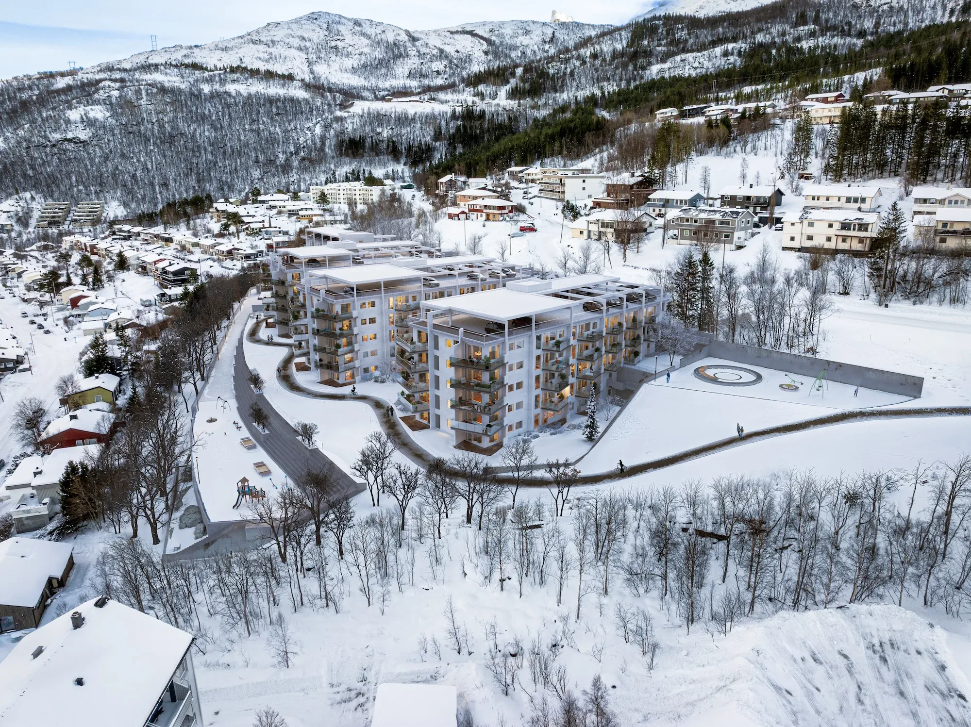 Flyfoto av moderne boligblokker omgitt av snødekt landskap og åser i et boligområde.